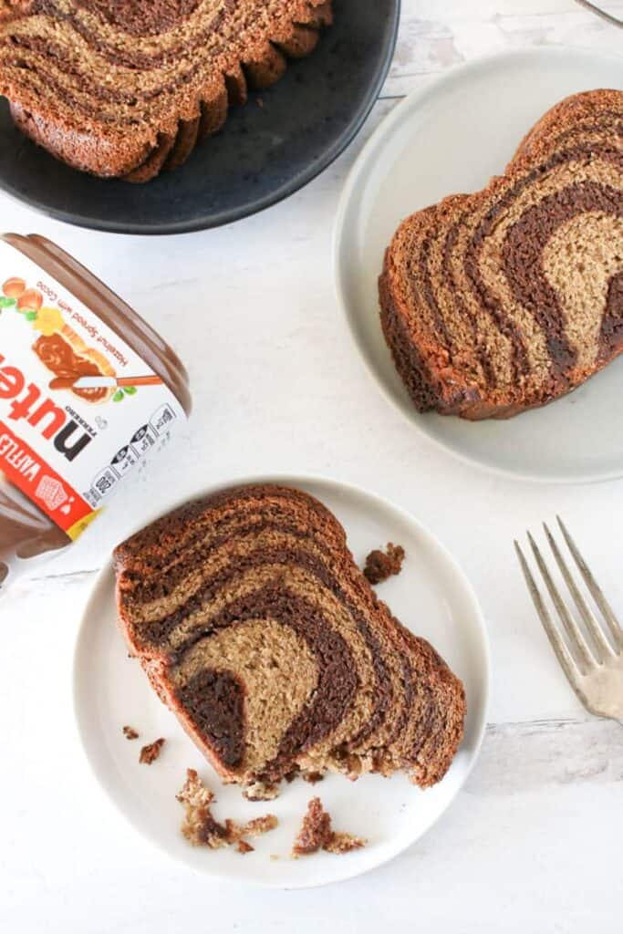 Slices of food processor nutella banana bread on 3 different plates with 1 slice being slightly eaten with a nutella jar and antique fork off to the side
