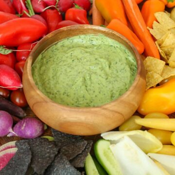 Angle of green goddess dip in wooden bowl surrounded by colorful vegetables