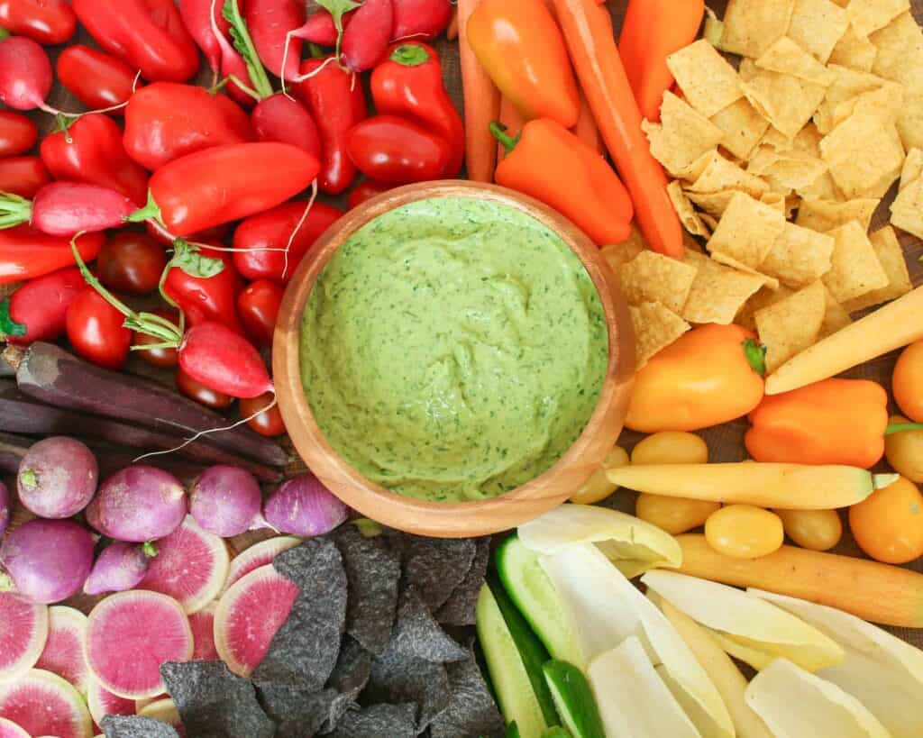 Overhead of green goddess dip in wooden bowl surrounded by colorful vegetables