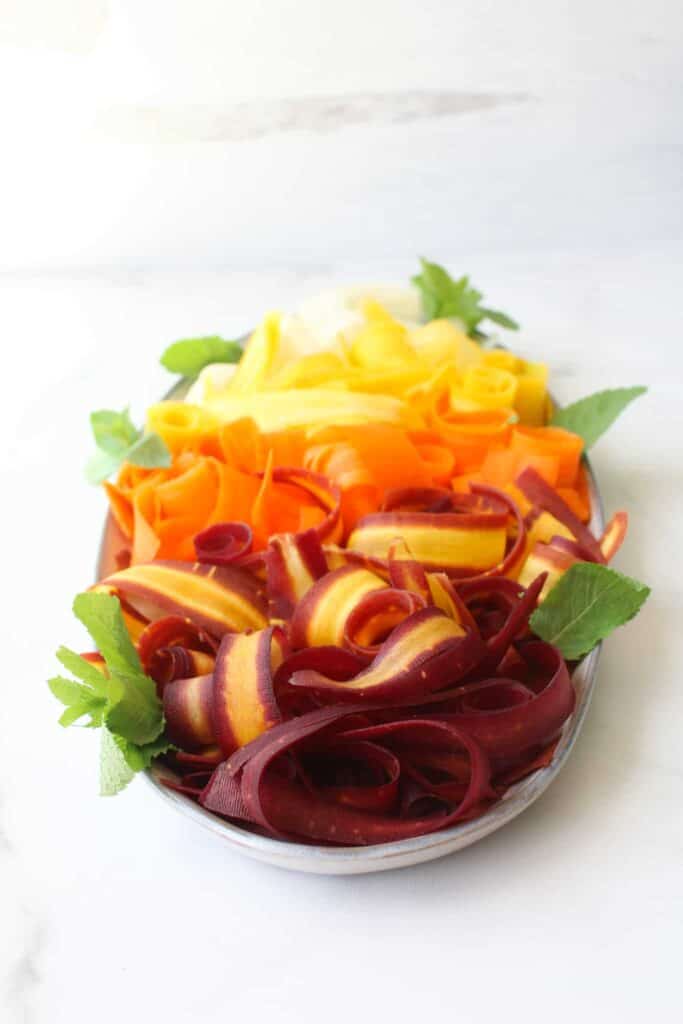 Angle shot of raw rainbow ribbon salad with only carrots and mint, ombree with purple first, orange, yellow and white last