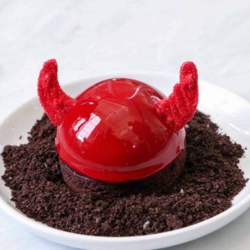 Straight on photo of Halloween Nutella Devil Entremet on a bed of salted oreo dirt in a circule white dish on a marble background