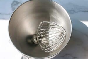 Metal mixing bowl + whisk attachment that's cold on a marble background