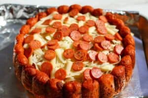 Pizza cake on a small baking sheet with aluminum foil with unbaked shredded mozzarella cheese, mini pepperoni and oregano