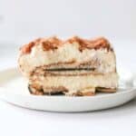 A slice of milano tiramisu on a small white plate. You can see cookie layer and vividly and cocoa powder is dusted on top.