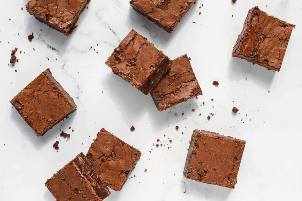 multiple brownie squares on a white marble background with brownie crumbs spread out/