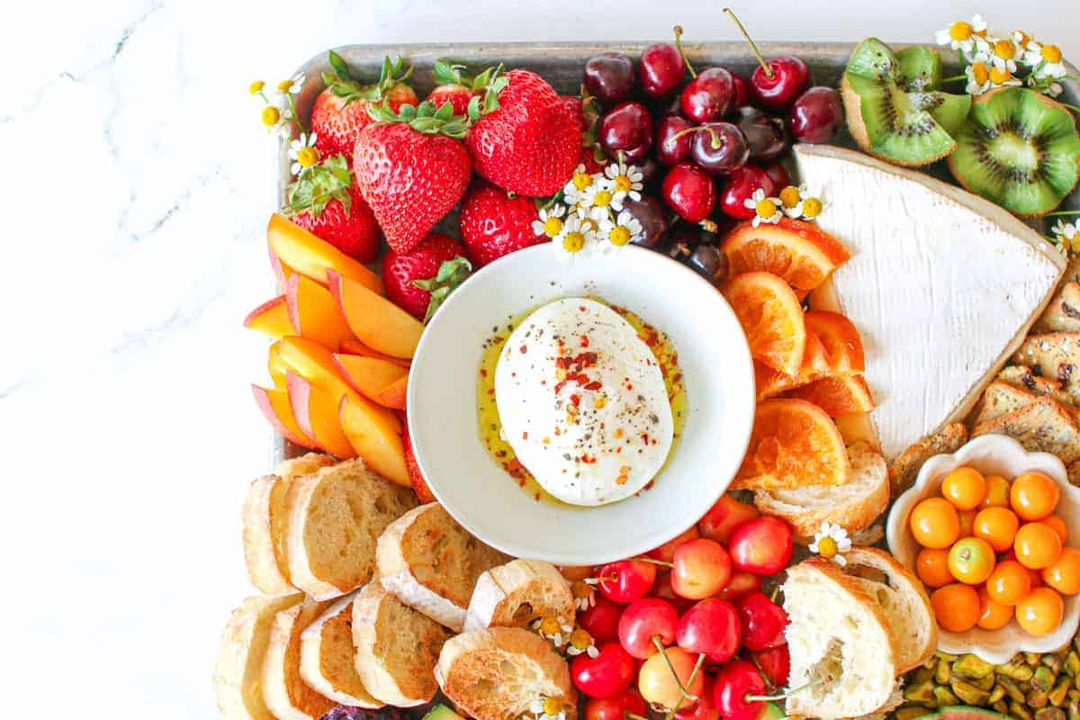 Close up of the Trader Joe's Summer Fruit & Cheese Board. The photo focuses on the upper middle part. It sits on a white marble background.