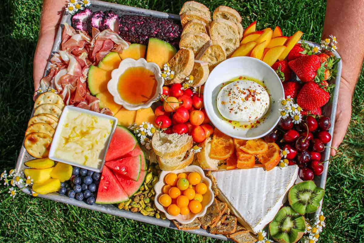 Trader Joe's Summer Fruit & Cheese Board being held in two hands outside by green grass