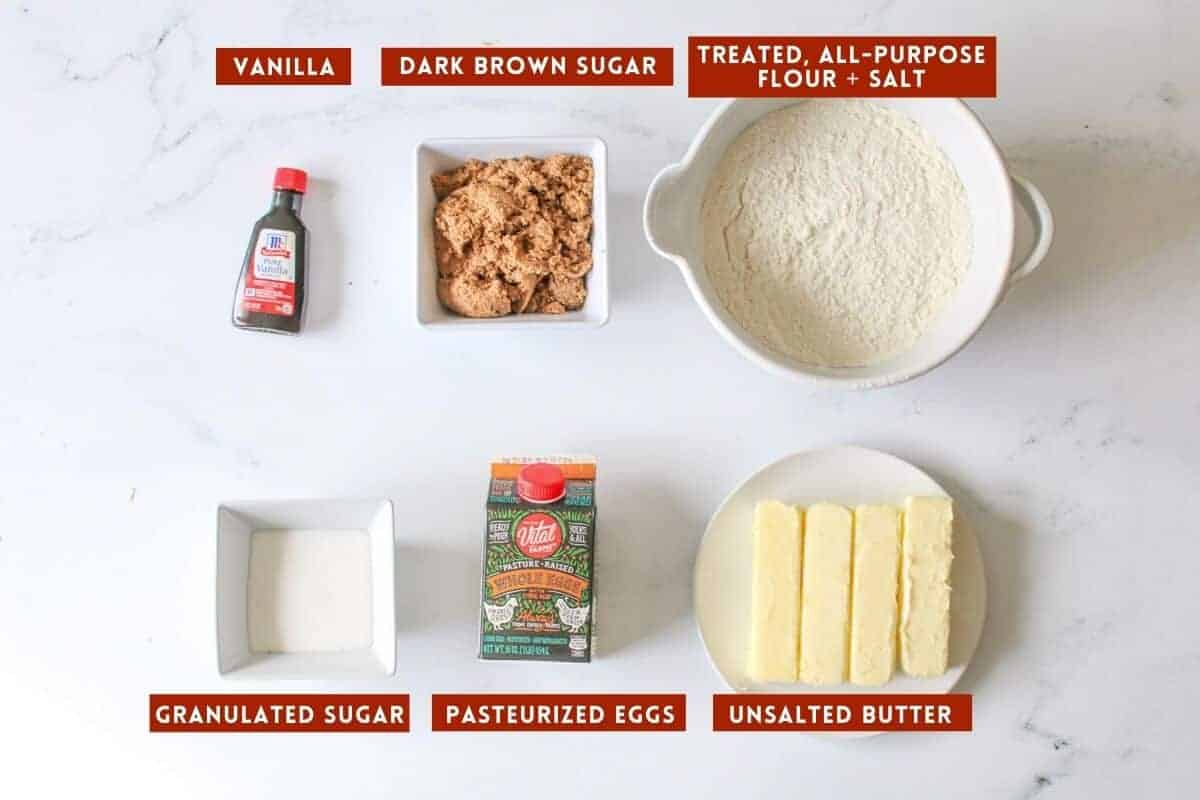 Edible cookie dough ingredients on a white marble background with a red box with white text on the inside labeling each ingredient.
