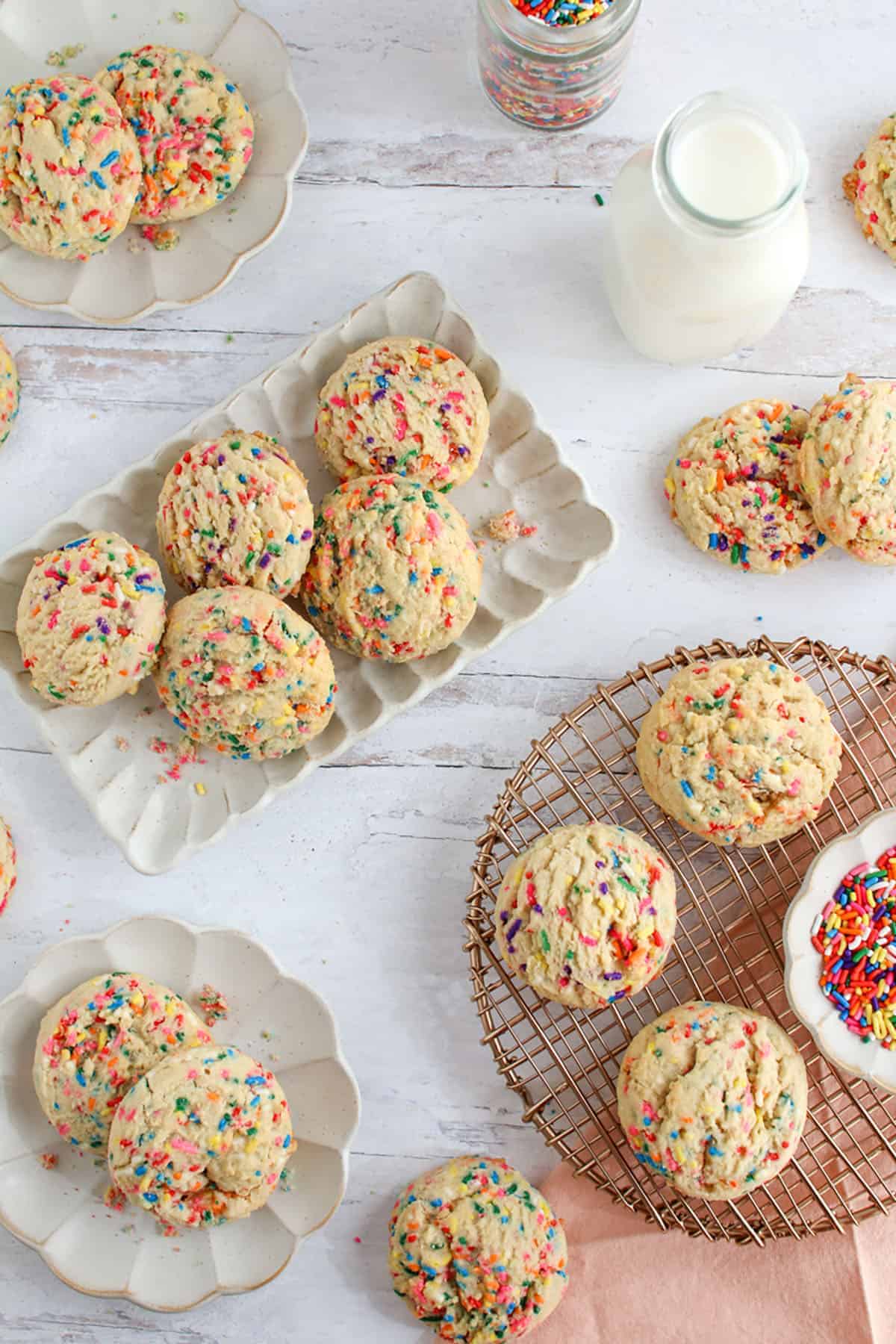 A bunch of High Altitude Funfetti Sugar Cookies on different plates and background with a milk bottle and small jar full of sprinkles.