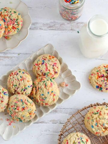 A bunch of High Altitude Funfetti Sugar Cookies on different plates and background with a milk bottle and small jar full of sprinkles.