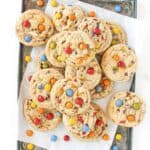 High Altitude M&M Cookies on a starburst sheet pan with white parchment paper and scattered m&ms