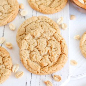 Close up of high altitude peanut butter cookies on a white wood board with peanuts surrounding.