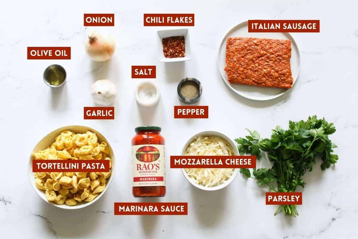 Baked Tortellini with Sausage Ingredients on a white marble background. Each ingredient is labeled with red rectangle with white text in all caps.