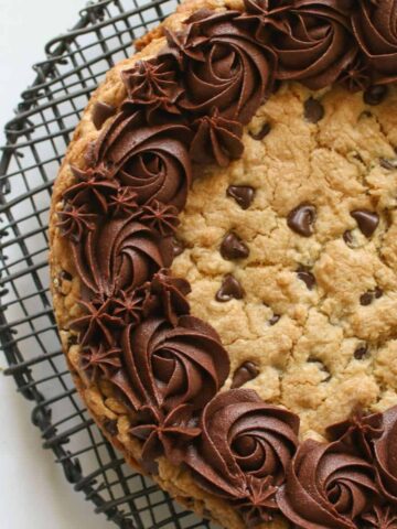 Overhead of Chocolate Chip Cookie Cake on a black wire rack on a white marble background. The cookie cake is slightly cut off.