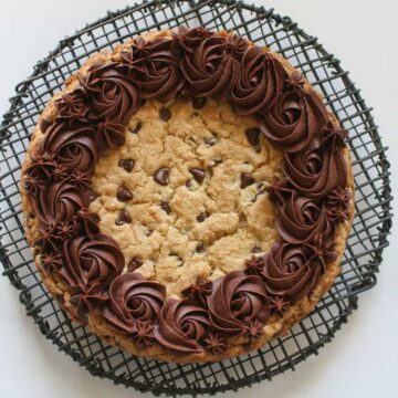 Overhead of Chocolate Chip Cookie Cake on a black wire rack on a white marble background.