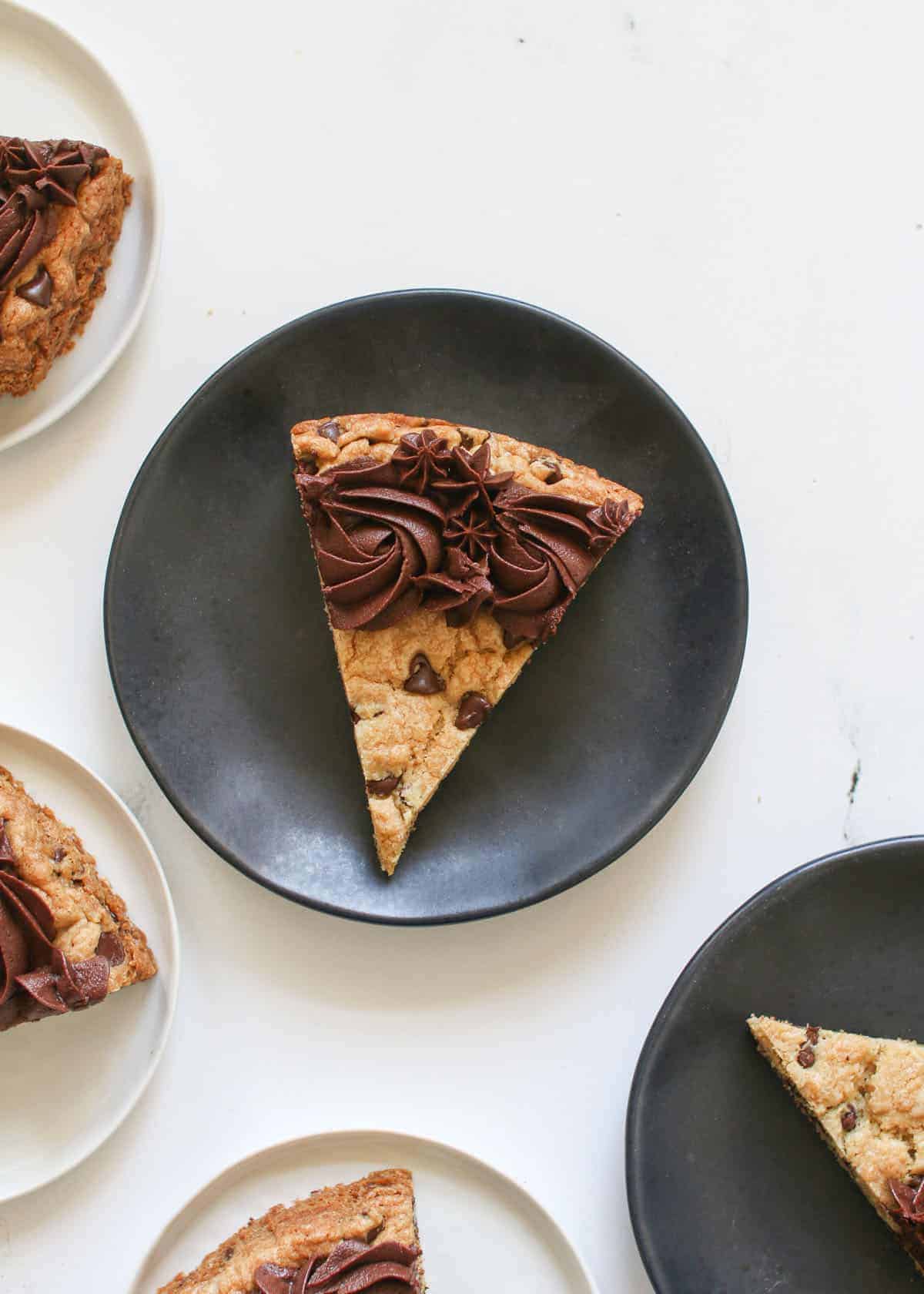 Sliced chocolate chip cookie cake on white and black small plates on a white marble background