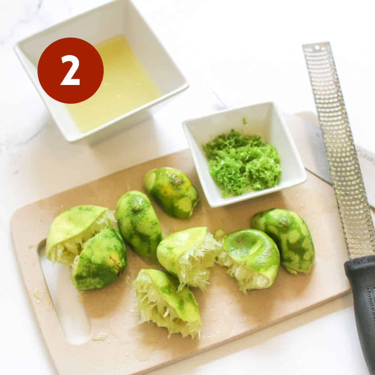 Several half limes juiced and zest on a small cutting board with small white bowls and a zester on the side on a white marble background. In the upper left corner is a white '2' in a dark red circle in an upper left corner.