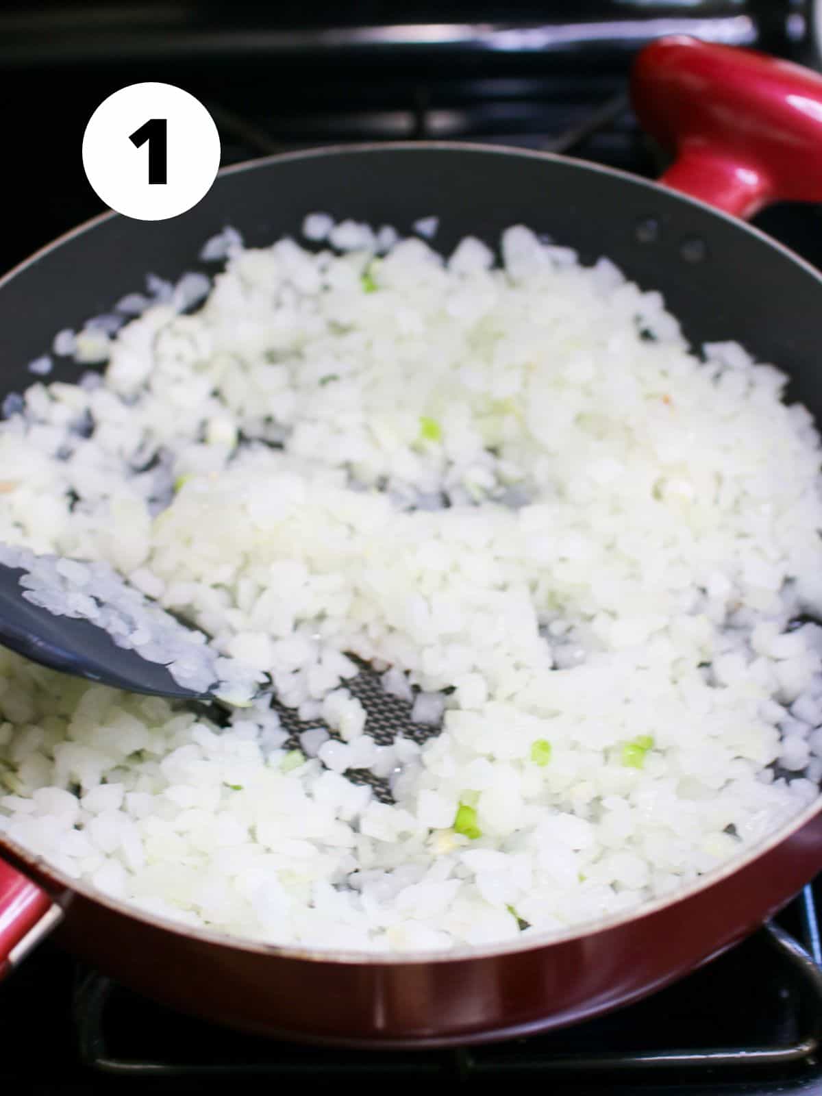 A large red skillet with chopped onions and a silicone turner on the stove top. In the upper left corner is a white circle with a black '1'. 