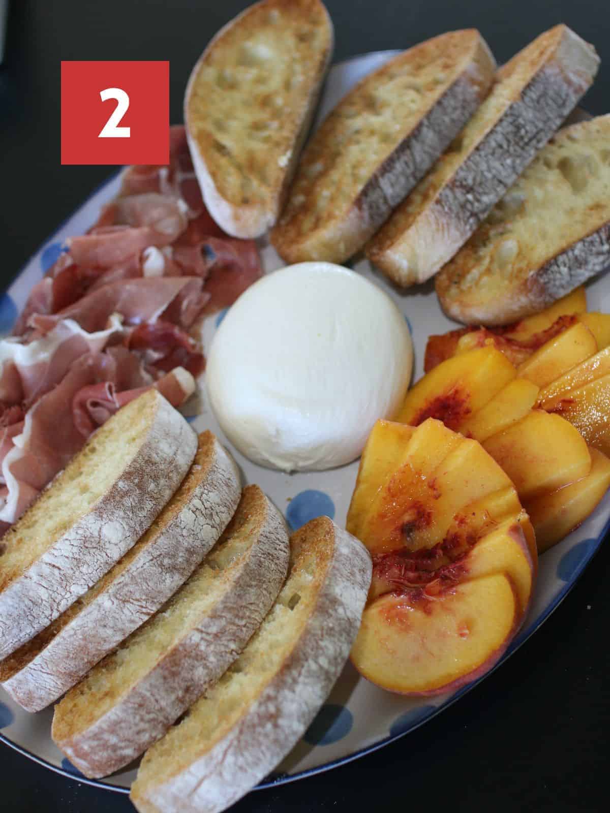 Burrata, Prosciutto, and Peaches Plate without garnishes on a white platter with blue dots on a black table. In the upper left corner is a red box with a white '2' in the center. 