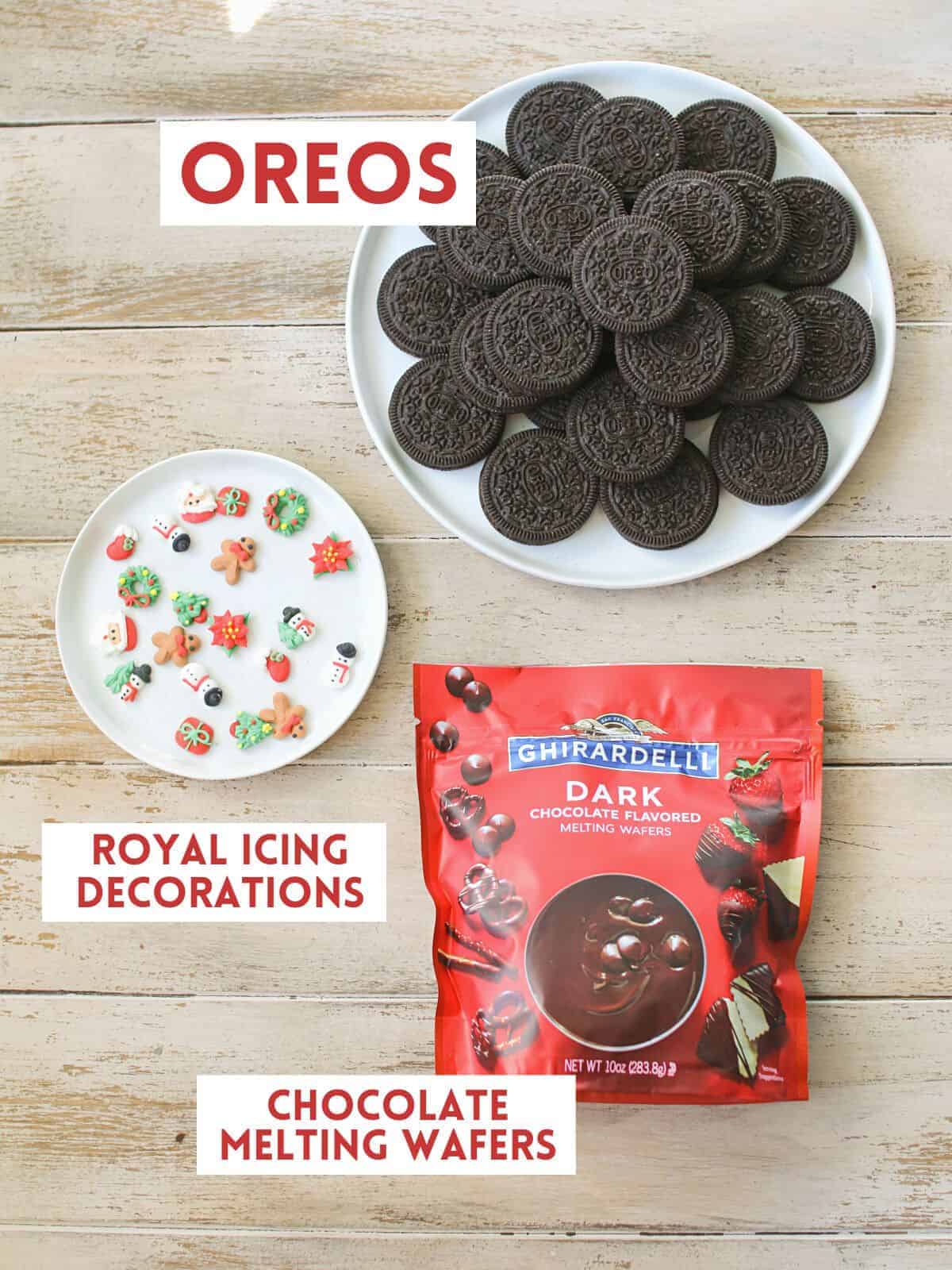 A white plate with oreos stacked, a smaller white plate with a variety of Christmas shaped royal icing pieces and a red bag of chocolate melting wafers. Each item is labeled with a white rectangle box with text in all caps in dark red on a light wood plank background.