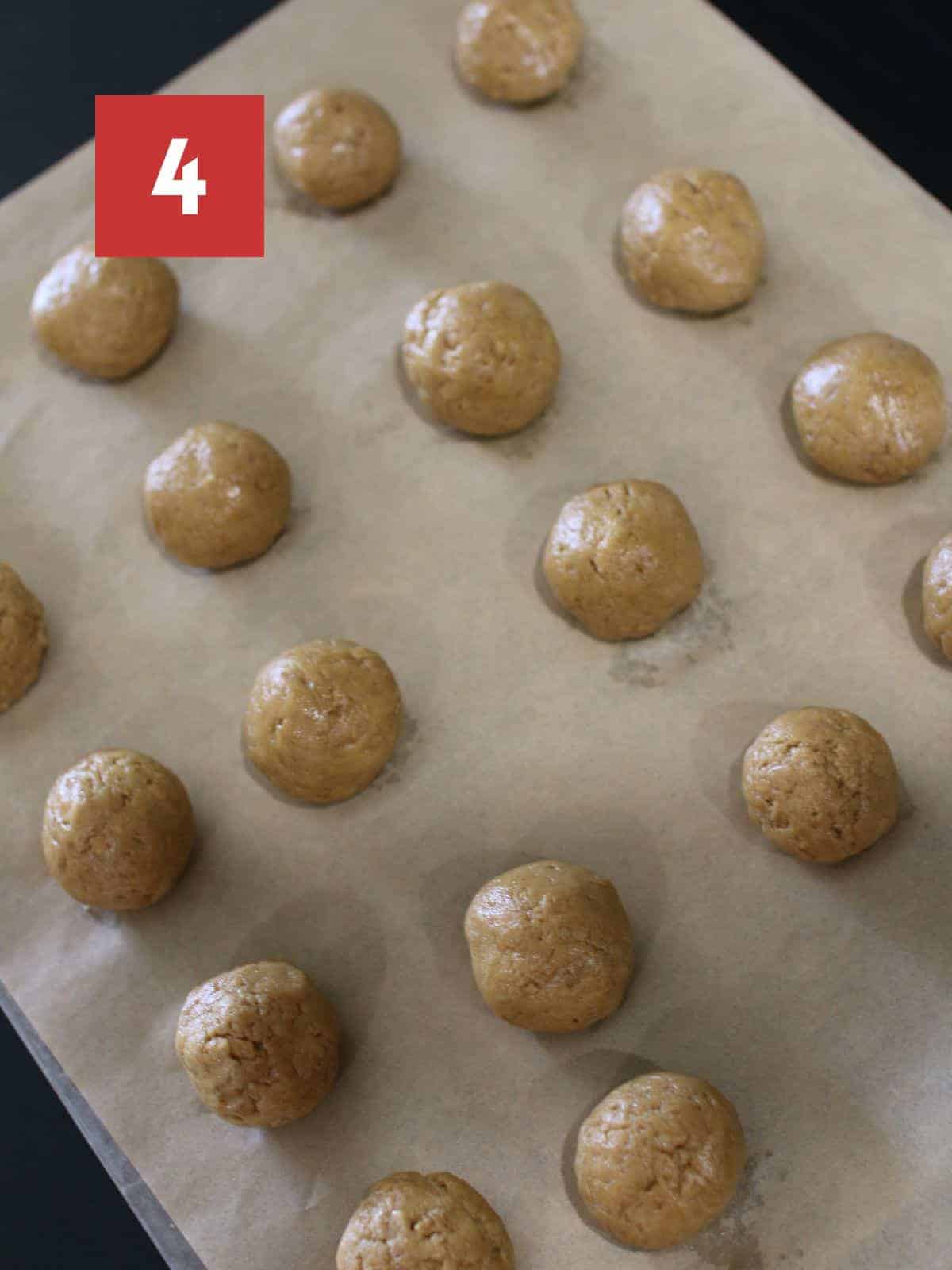 Rolled gingerbread truffles on a brown parchment lined baking sheet that sits on a black table.  In the upper left corner is a dark red square and a white '4' in the center.