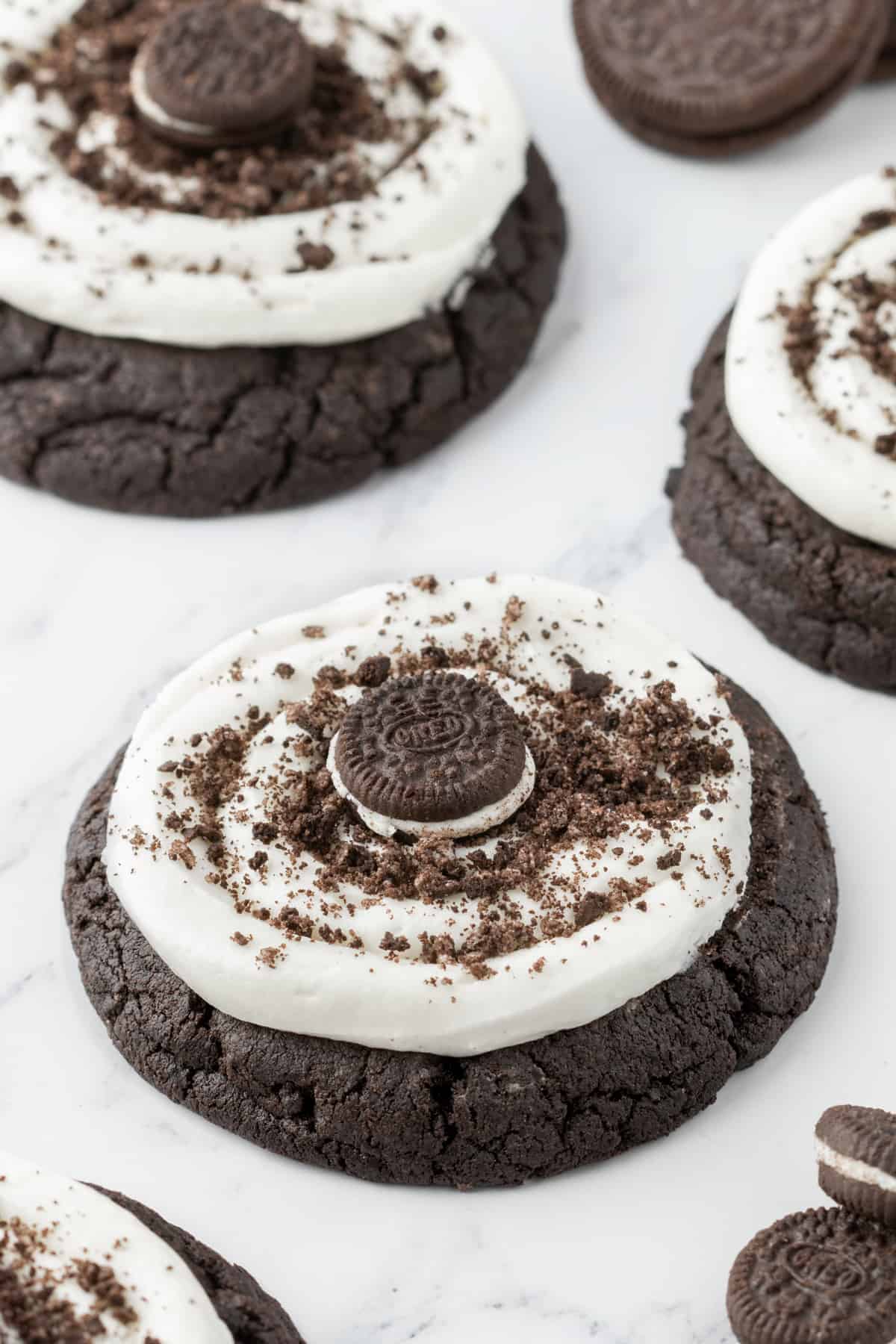Angled Oreo Crumbl Cookies on white marble background. Each cookie is topped with crumbled oreos and a mini oreo cookie.