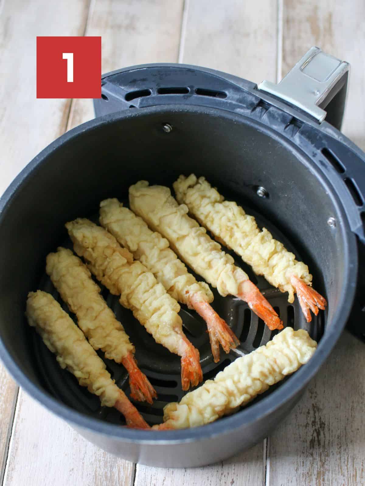 Frozen tempura shrimp placed in an air fryer basked. In the upper left corner is a white '1' in a dark red square.