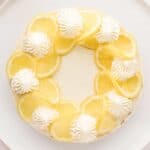 Overhead No Bake Lemon Cheesecake on a white platter. The top is decorated with piped whipped cream and twisted lemon slices.