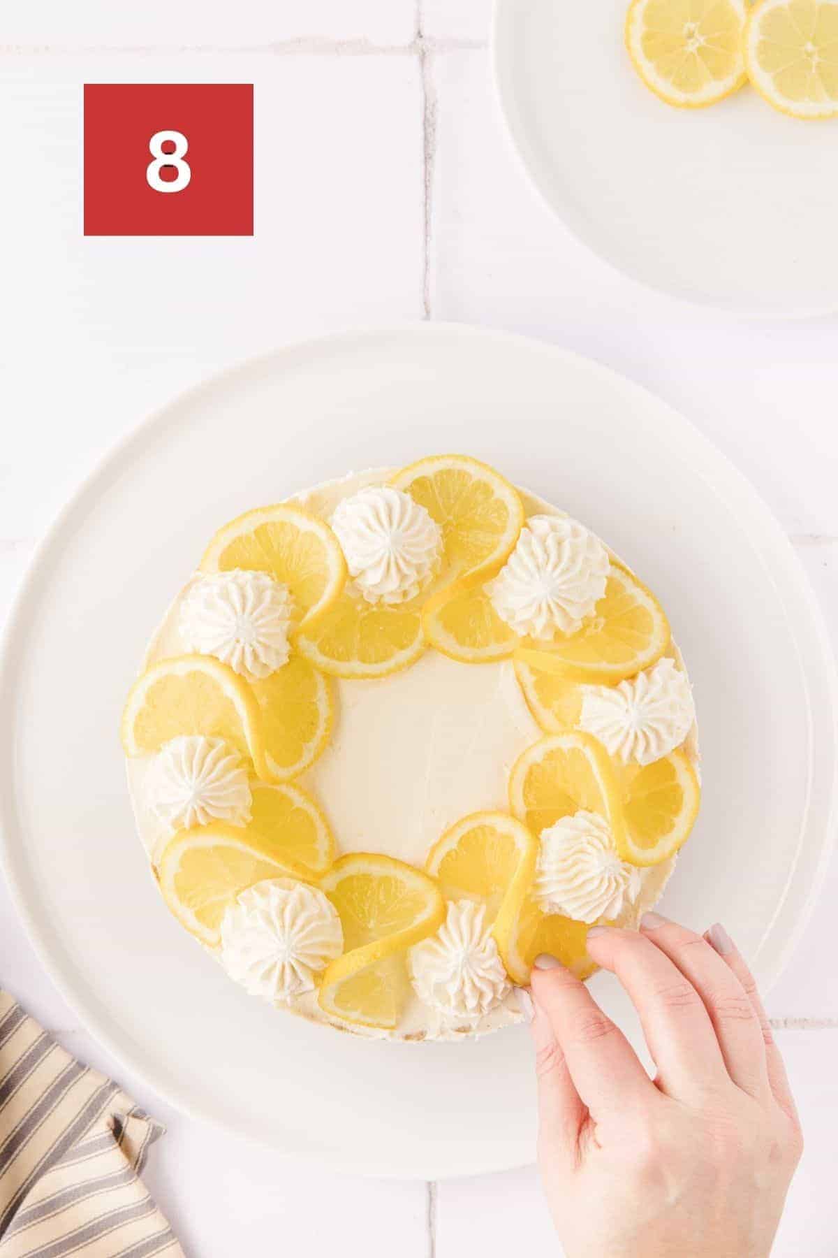 A hand placing lemon slices on top of the no bake lemon cheesecake. In the upper left corner is a dark red square with a white '8' in the center.
