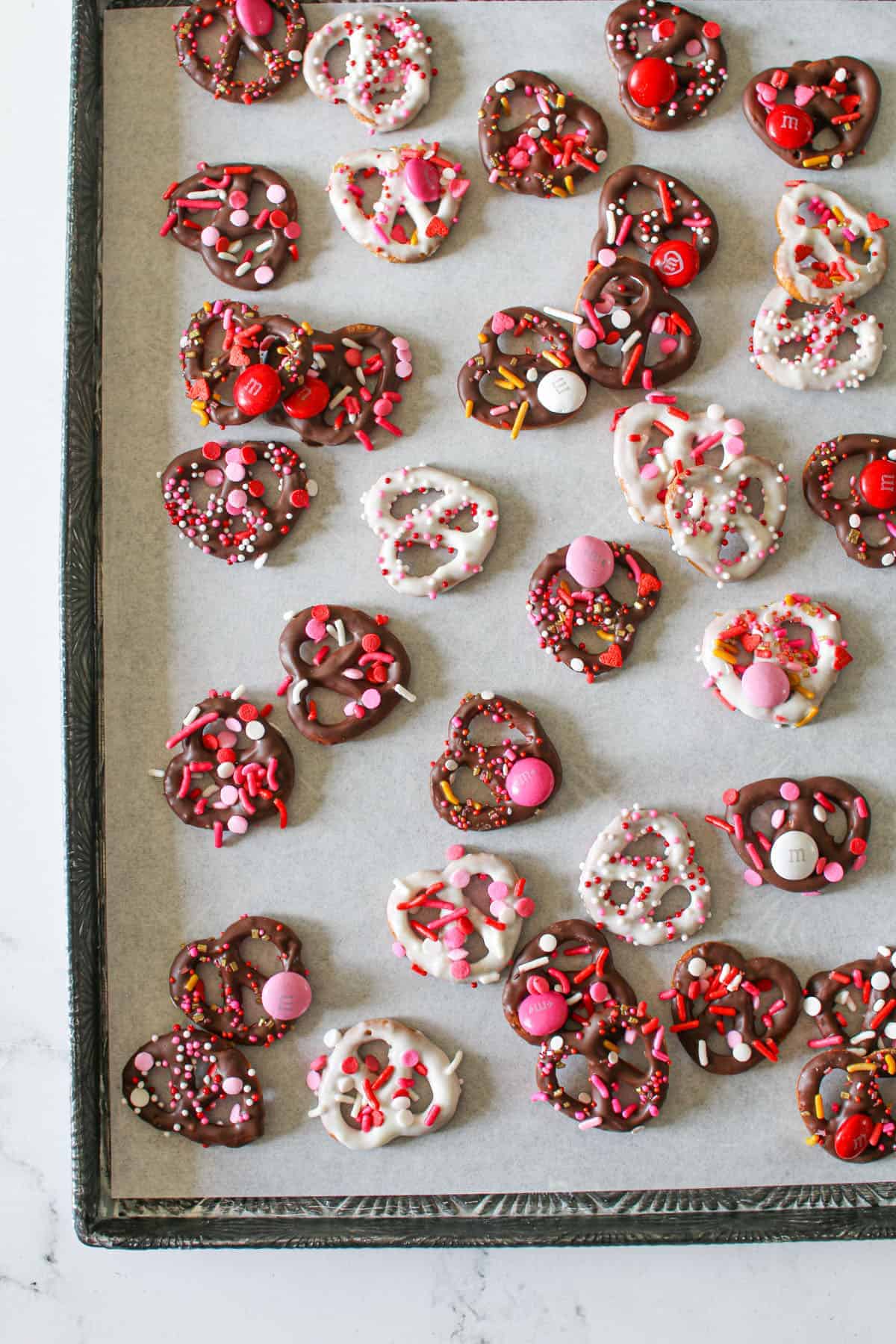 White and Dark Chocolate Valentine's Day Chocolate Covered Pretzels on white parchment paper on a starburst baking pan on a white marble background.