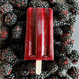 A blackberry popsicle surrounded by fresh blackberries.