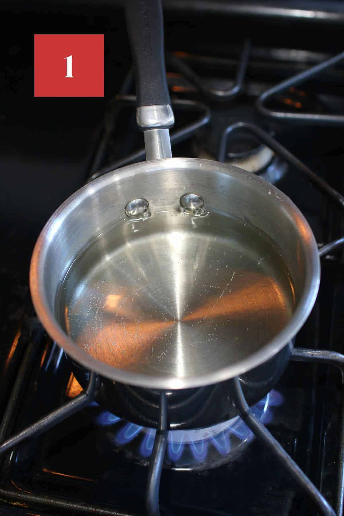 A small sauce pan with simple syrup on the burner. In the upper left corner is a dark red square with a white '1' in the center.