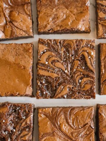 High Altitude Brownies in rows and columns (3x3) with a little space in between each square on a white marble background. 3 variations of brownies include plain, salted caramel and nutella.