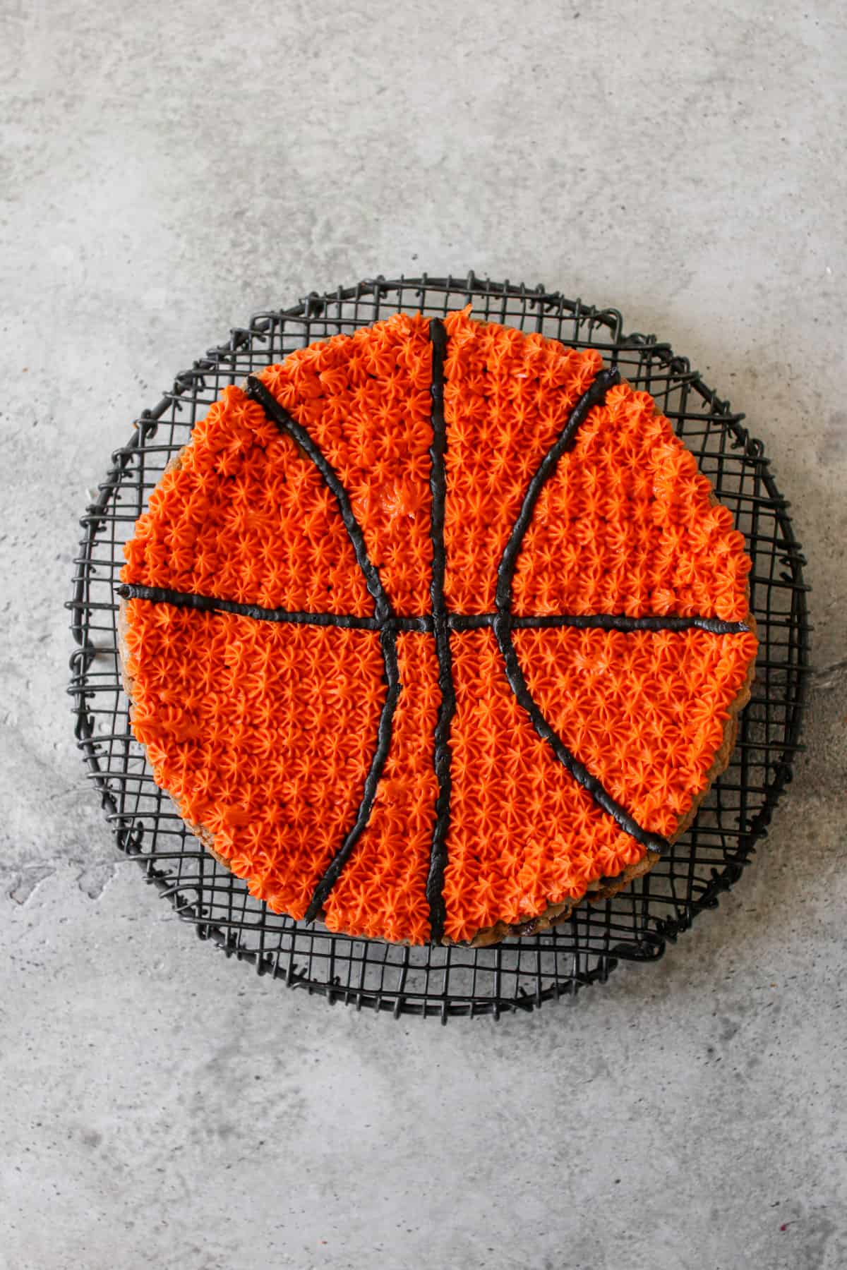 A baseball decorated cookie cake on a black wire trivet on a cement background.