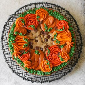 Overhead of Fall Cookie Cake with decorate buttercream pumpkins on a black wire trivet. The trivet sits on a cement background.