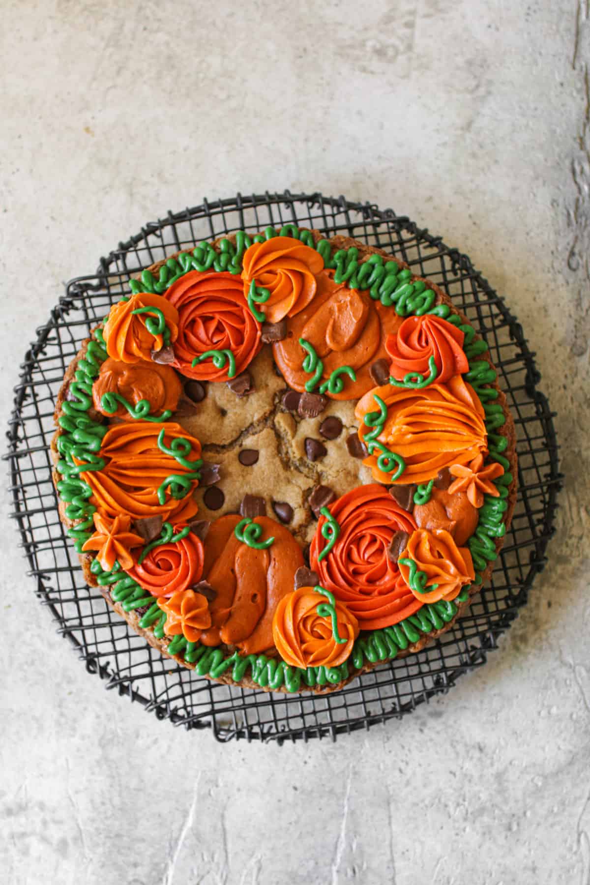 Overhead of Fall Cookie Cake with decorate buttercream pumpkins on a black wire trivet. The trivet sits on a cement background.