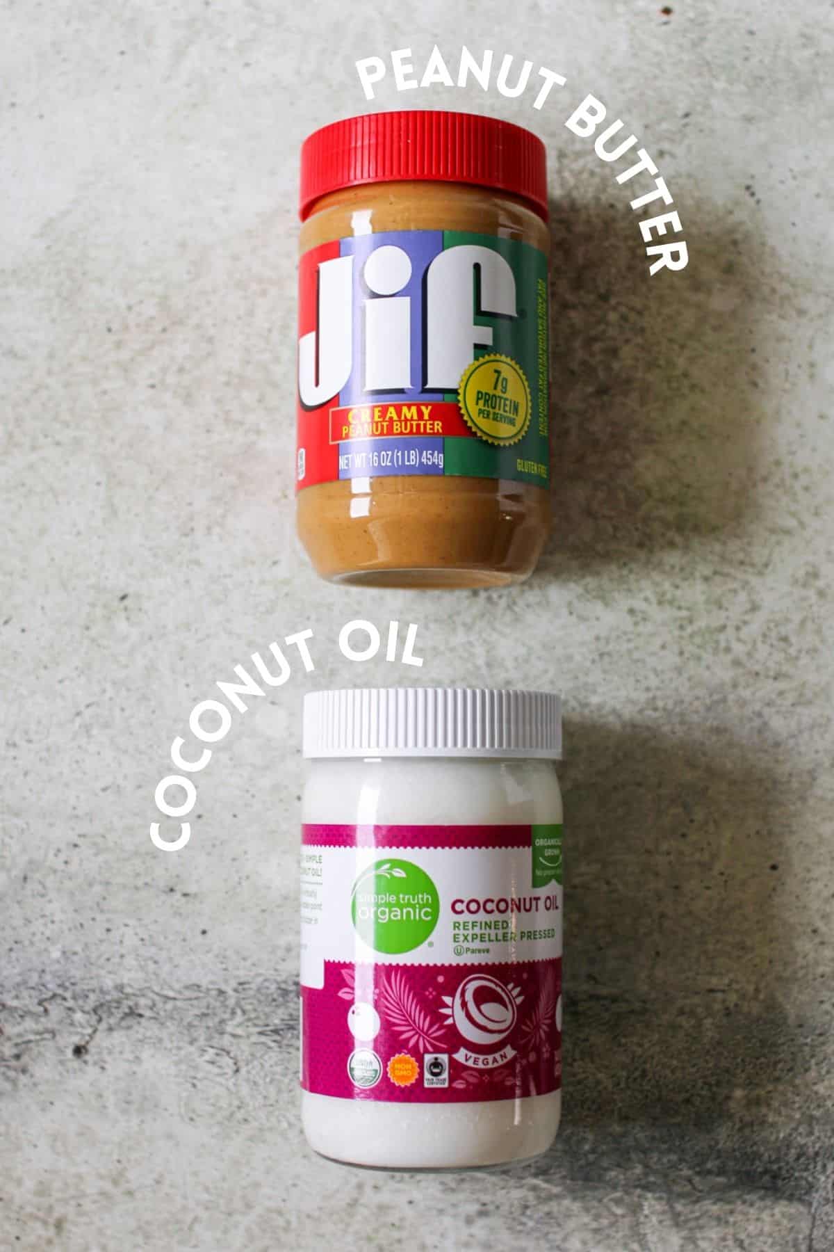 A jar of peanut butter and a jar of coconut oil on a cement background. Each it labeled with white text in alls caps.