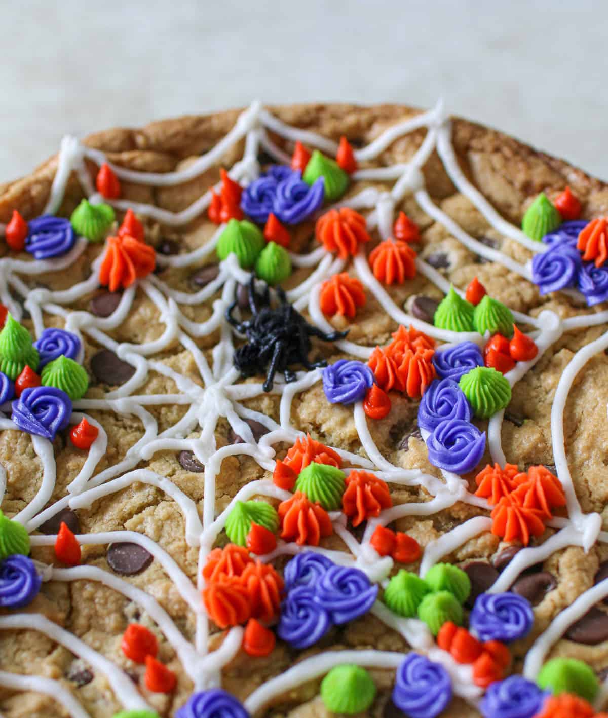 Angled close up of Spider Web Cookie Cake decorate with a white web, small colorful scattered flowers  on a stone background.