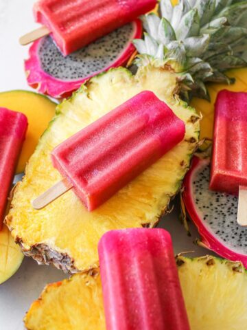 Angle of tropical Popsicles on a variety of sliced tropical fruit - pineapple, mango and dragon fruit on a white background.