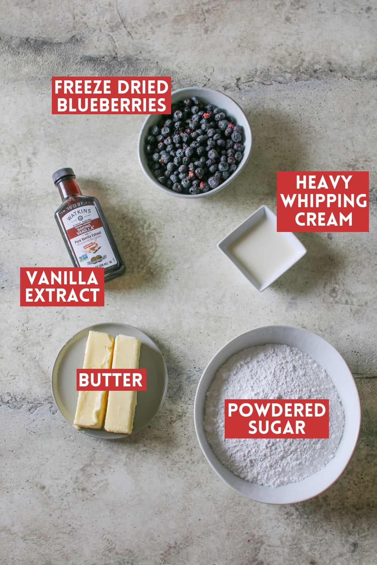 Blueberry Buttercream ingredients on a cement background. Each ingredient is labeled with a dark red rectangle with white text in all caps.
