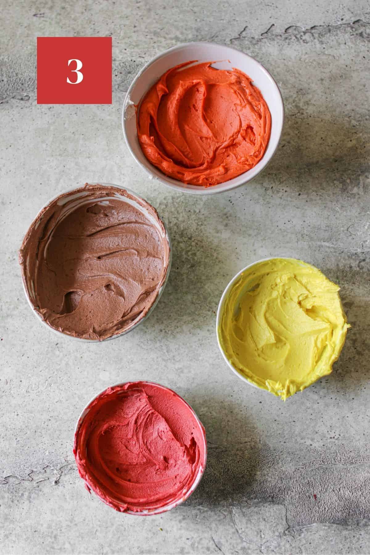 Brown, orange, red and yellow buttercream in separate bowls on a stone background. In the upper left corner is a dark red square with a white '3' in the center.