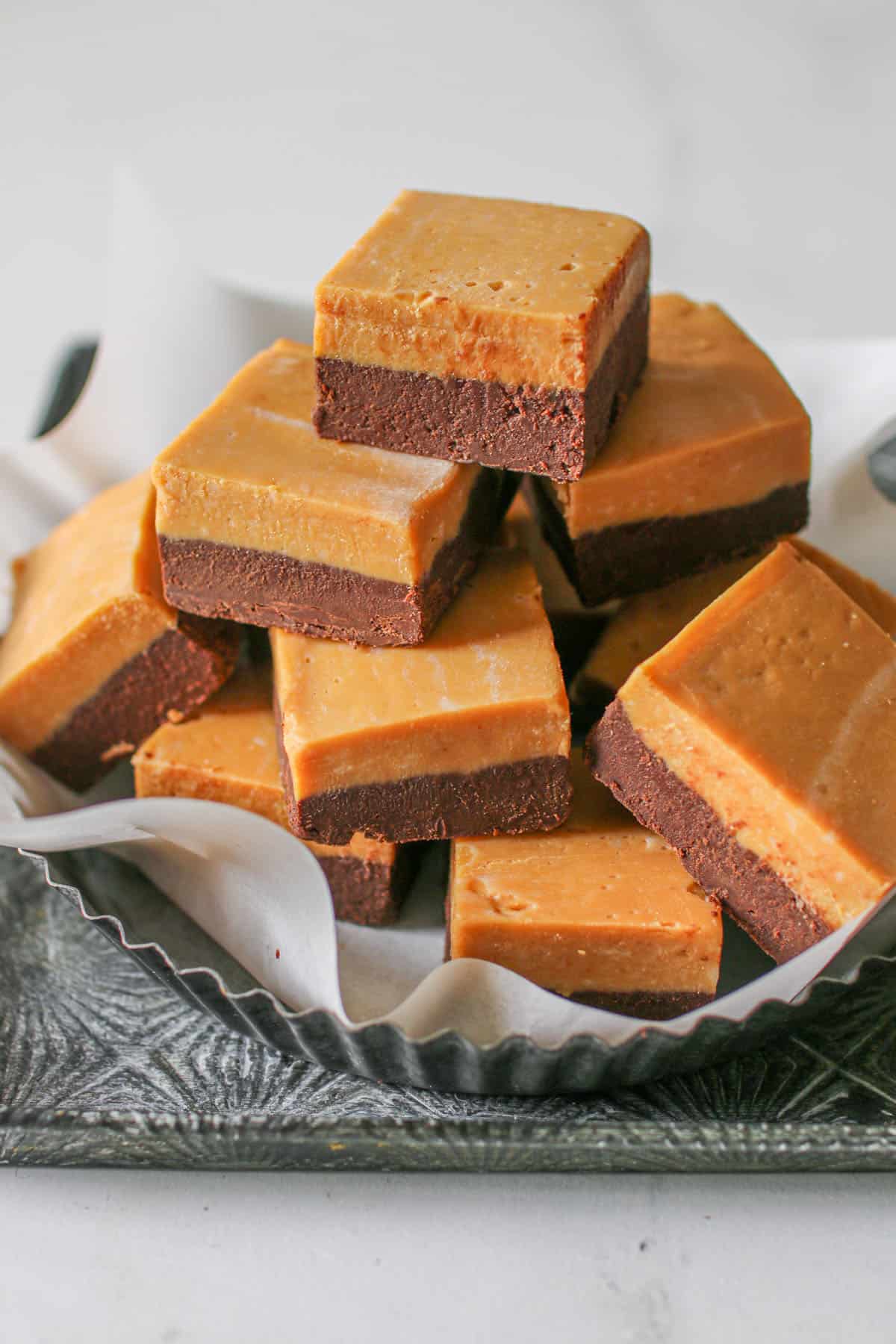 Two toned dulce de leche fudge stacked on top of each other on a metal baking tin with some white parchment paper.