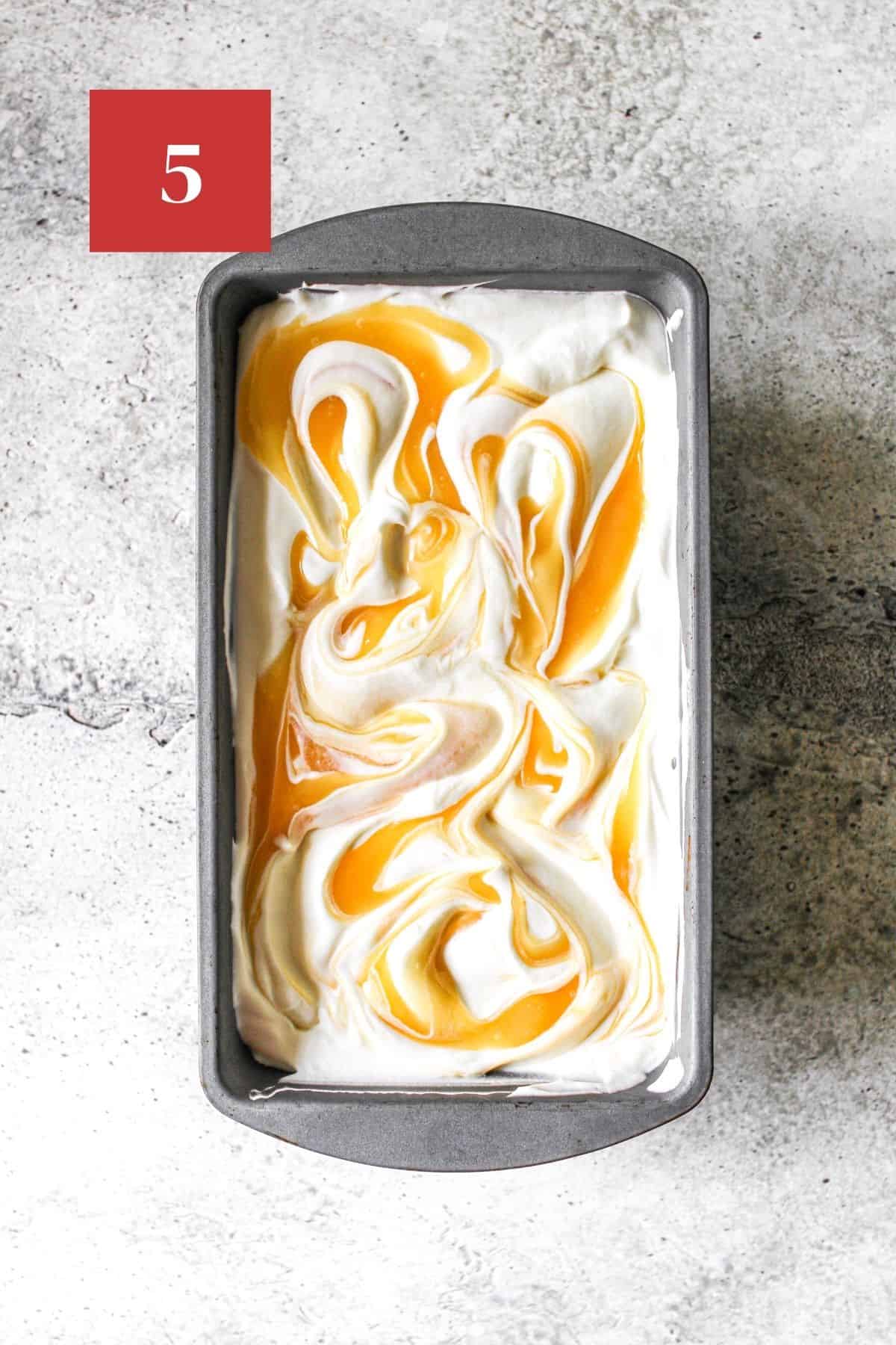 No Churn Lemon Ice Cream in a metal tin on a stone background. The ice cream has swirls of lemon curd.  In the upper left corner is a dark red square with a white '5' in the center.