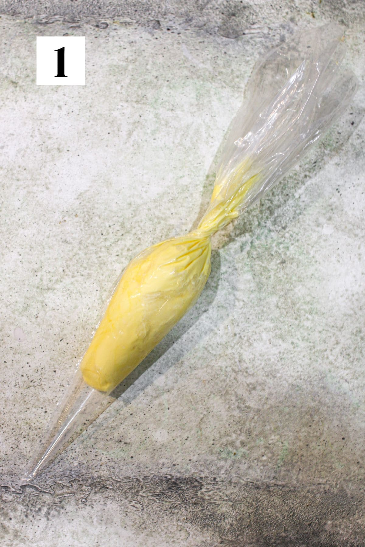 A piping bag filled with room temperature butter. It sits on a cement background. In the upper left corner is a white square with a black '1'.