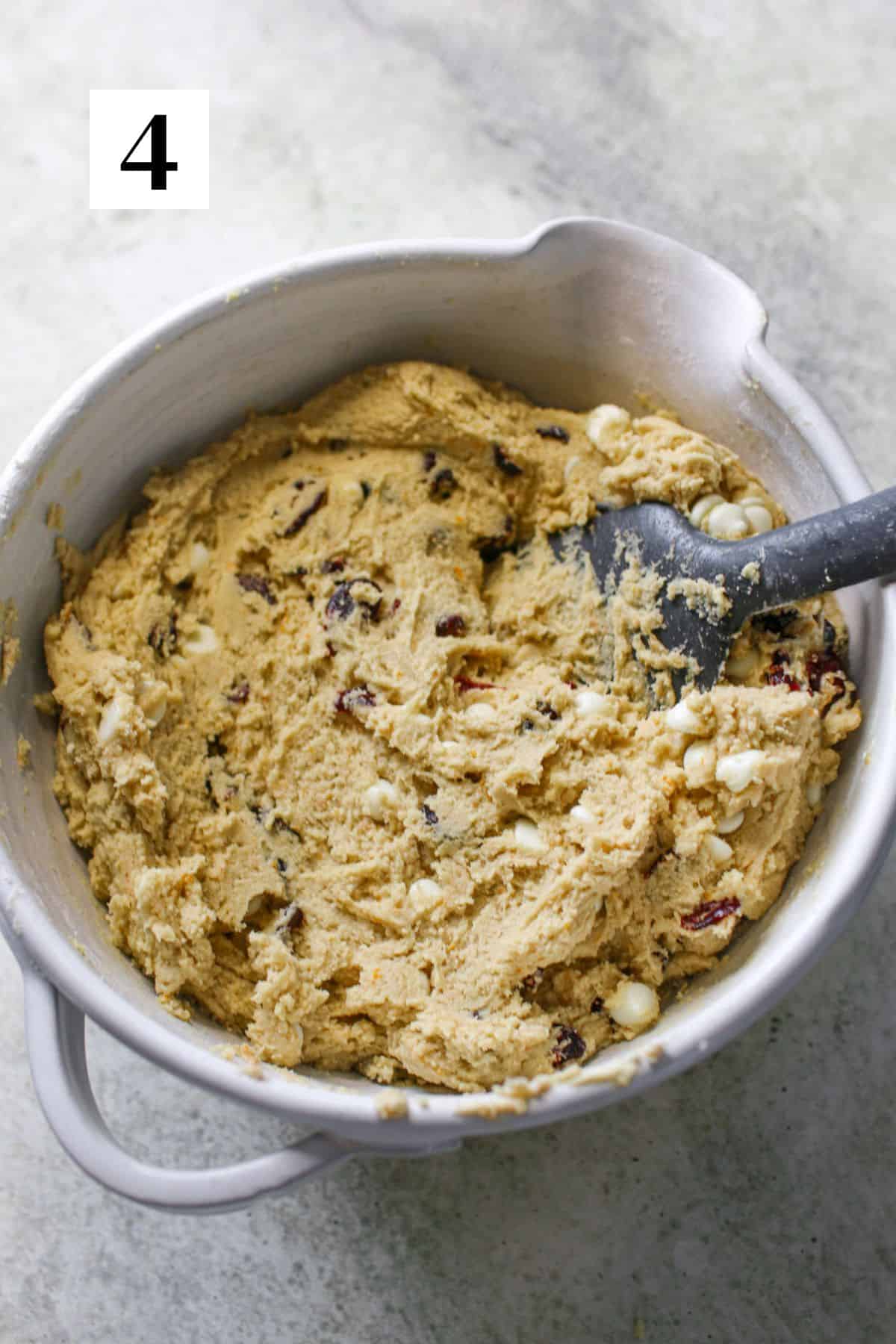 High Altitude White Chocolate Cranberry Orange Cookie dough in a white mixing bowl with a grey silicone spatula. In the upper left corner is a white square with a black '4'.